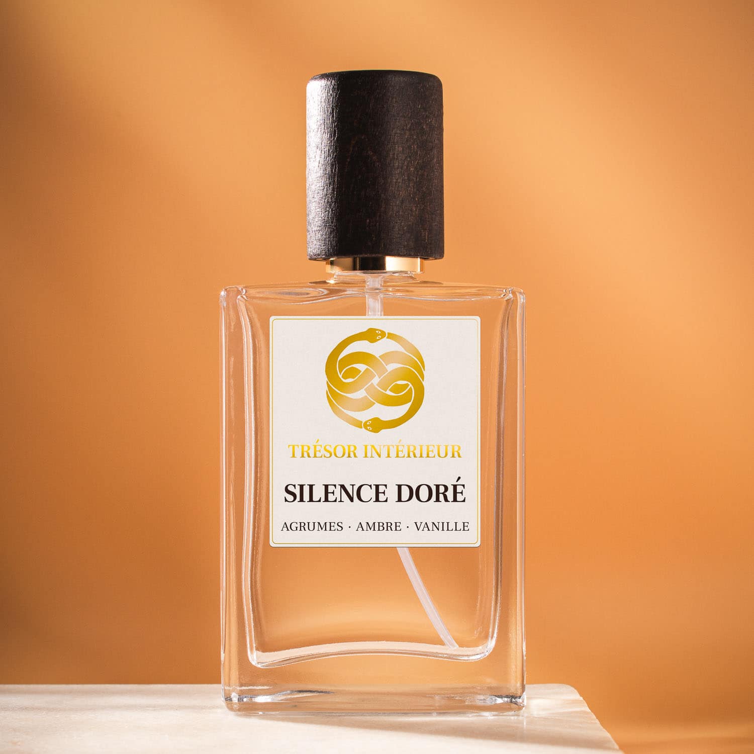 Flacon de spray parfum d’intérieur Trésor Intérieur « Silence Doré » 50ml, étiquette blanche et logo doré, fond orange.