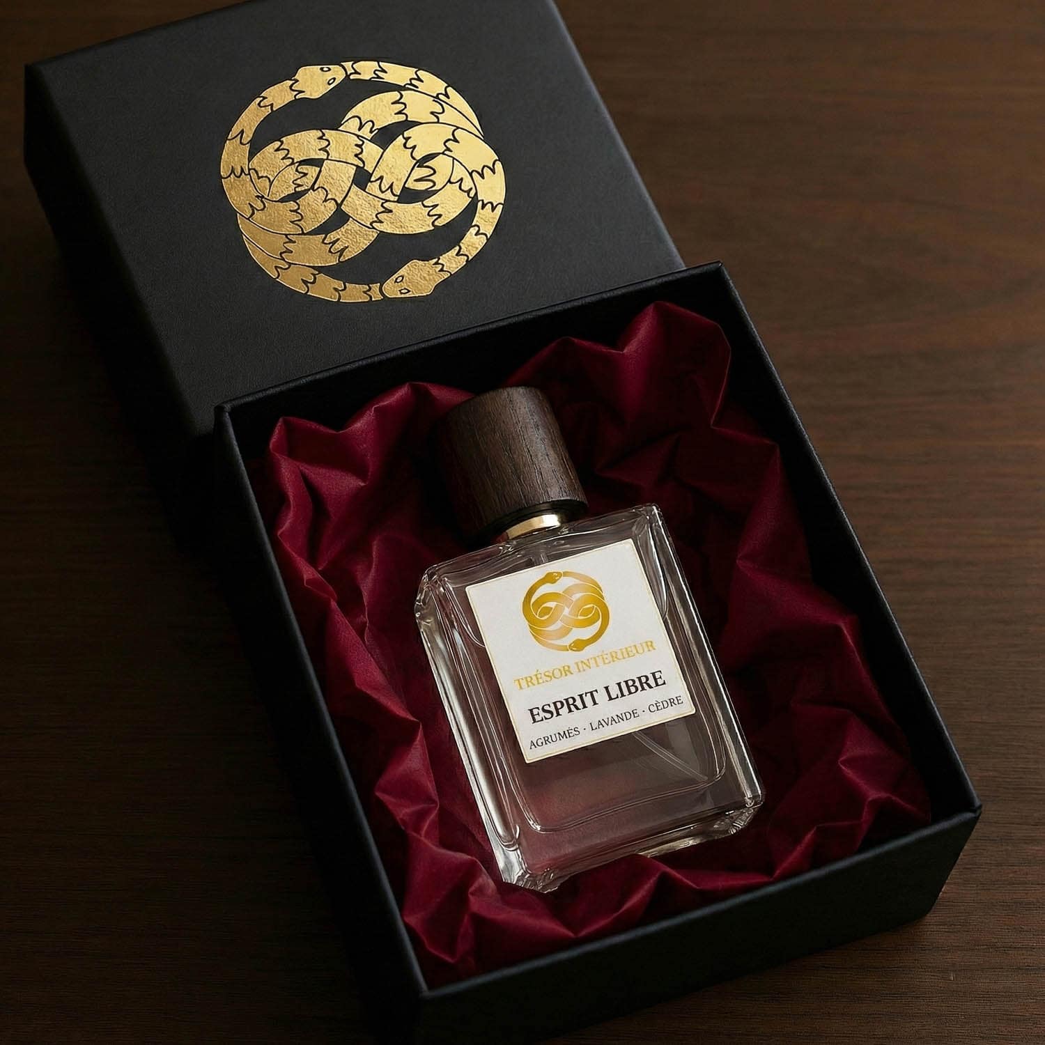 Flacon de parfum dans un coffret noir « TRÉSOR INTÉRIEUR » avec papier de soie bordeaux, posé sur une table en bois.